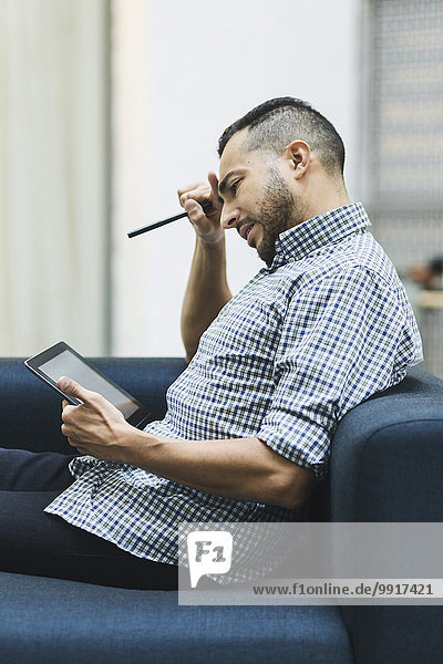 Besorgter Geschäftsmann mit digitalem Tablett auf dem Sofa im Büro