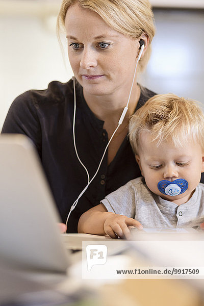 Mother with baby boy listening music on laptop at home