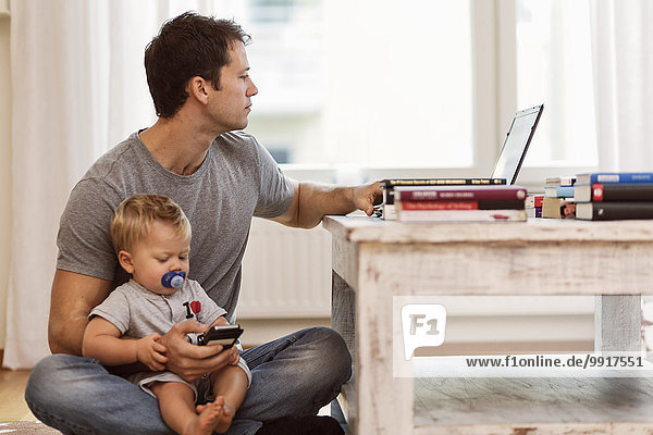 Mann  der den Laptop benutzt  während er den kleinen Jungen zu Hause hält.