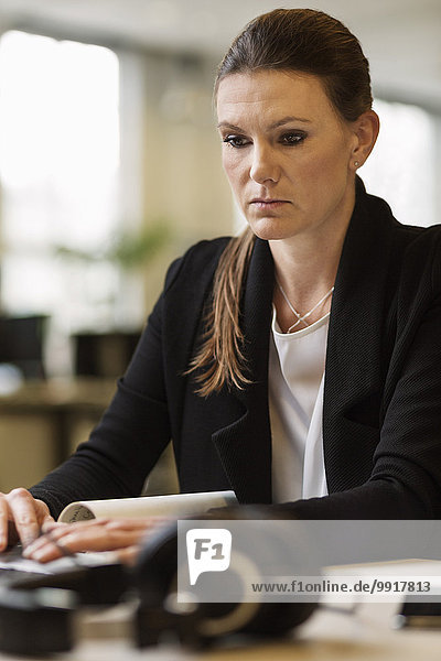 Serious businesswoman using laptop at desk in creative office