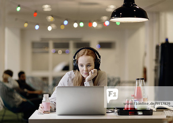 Geschäftsfrau hört Musik  während sie spät am Laptop im Kreativbüro arbeitet.