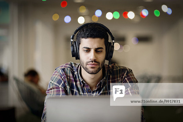 Geschäftsmann mit Kopfhörer bei der späten Arbeit am Laptop im Kreativbüro