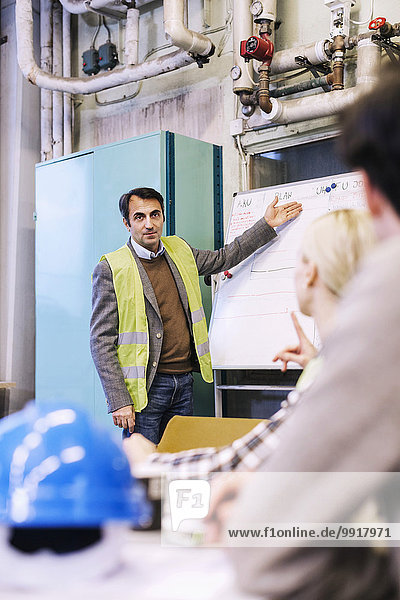Reife männliche Arbeitskraft diskutiert Plan auf Whiteboard mit Kollegen in der Fabrik