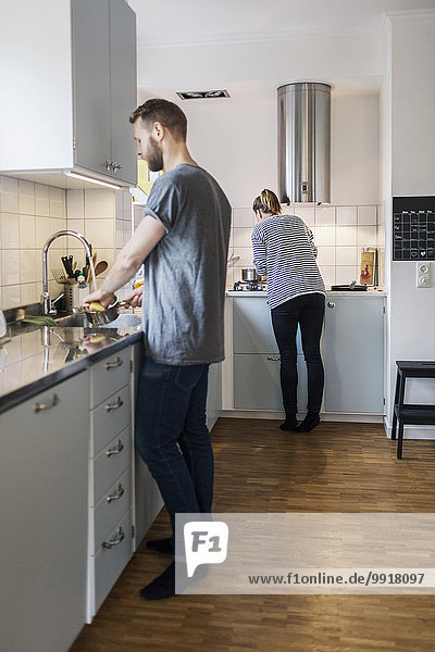 Mann wäscht Soßenpfanne  während Frau im Hintergrund in der Küche steht.