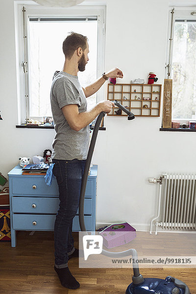 Full length of man vacuuming small shelves
