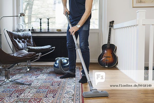 Low section of man vacuuming floor at home