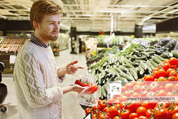 Junger Mann kauft frische Tomaten im Supermarkt