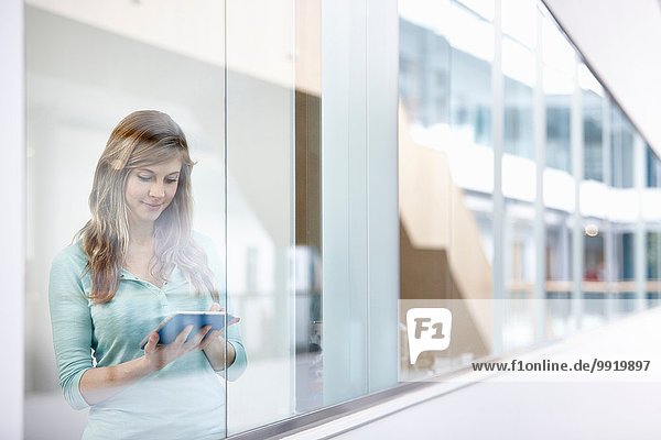 Geschäftsfrau mit digitalem Tablett hinter dem Bürofenster