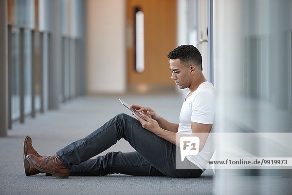 Junger Geschäftsmann im Büroflur sitzend mit digitalem Tablett