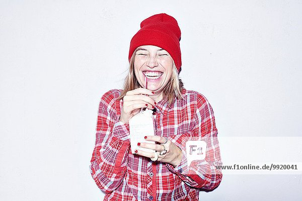 Studioporträt einer jungen Frau mit rotem Hut  die Saft trinkt.