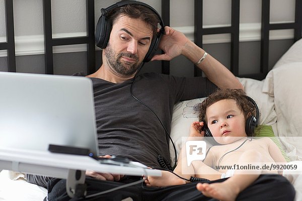 Vater und Tochter liegend im Bett und hören Musik über Kopfhörer.
