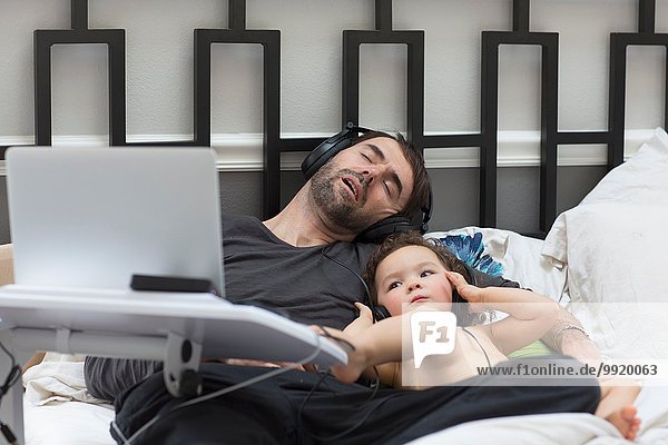 Weibliches Kleinkind hört Kopfhörermusik im Bett  während Vater schläft
