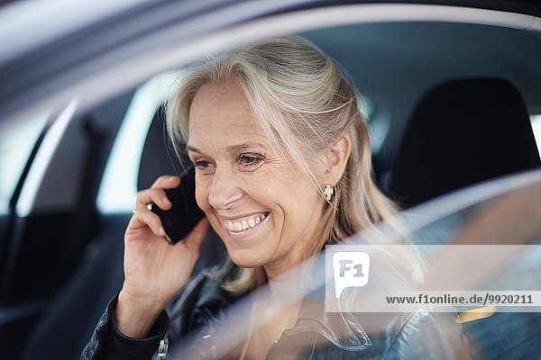Mature businesswoman chatting on smartphone in car