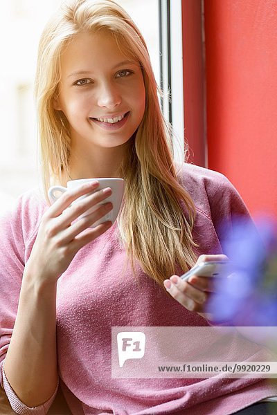 Porträt einer jungen Frau beim Kaffeetrinken mit dem Smartphone im Cafe