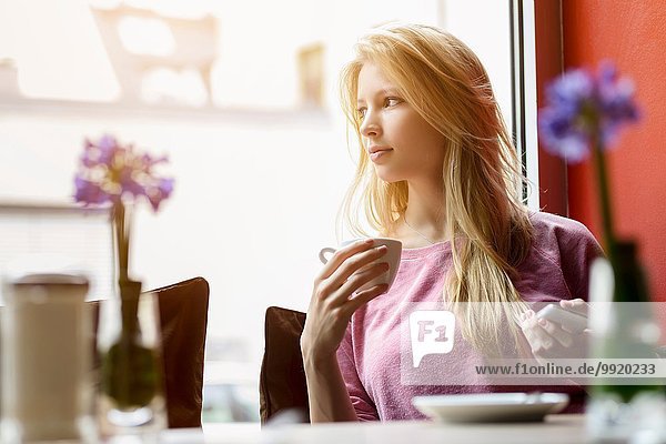 Junge Frau  die beim Kaffeetrinken aus dem Caféfenster schaut