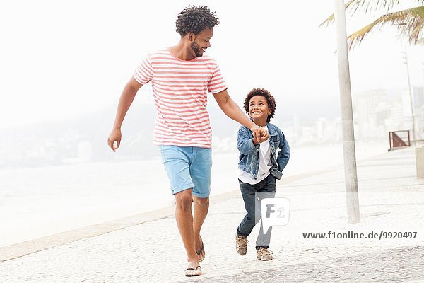 Vater und Sohn laufen Hand in Hand am Strand von Ipanema Rio De Janeiro Brasilien
