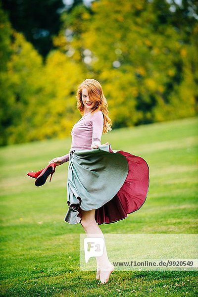 Portrait of young female dancer poised holding skirt and red high heels in park