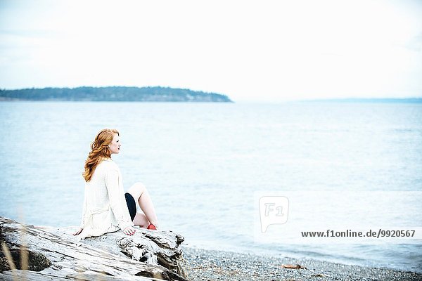 Young woman sitting on beach looking out to sea  Bainbridge Island  Washington State  USA
