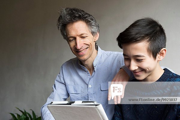 Vater und jugendlicher Sohn lesen digitales Tablett
