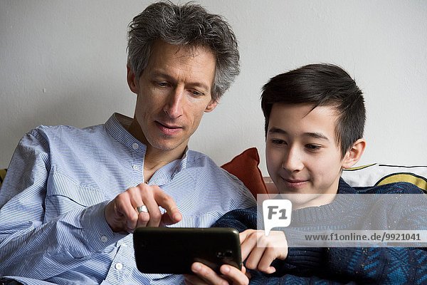 Teenage boy and father playing smartphone game on sofa