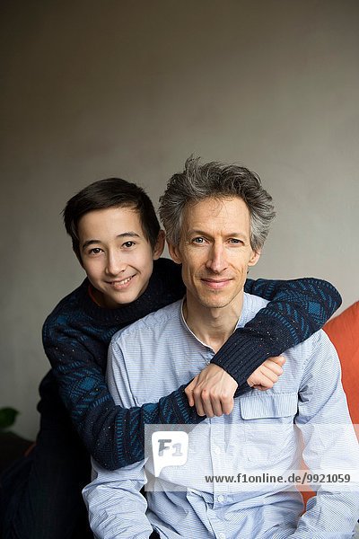 Portrait of teenage boy with arms around father on sofa