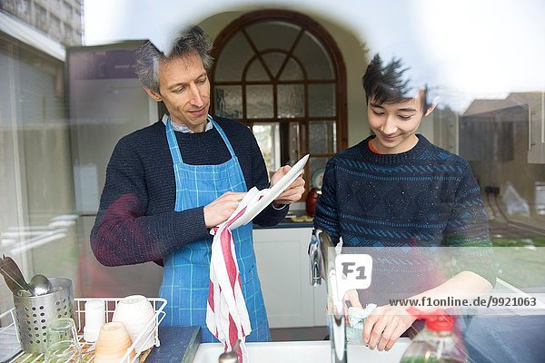 Blick durch das Fenster des Teenagers und Vaters beim Abwaschen in der Küche