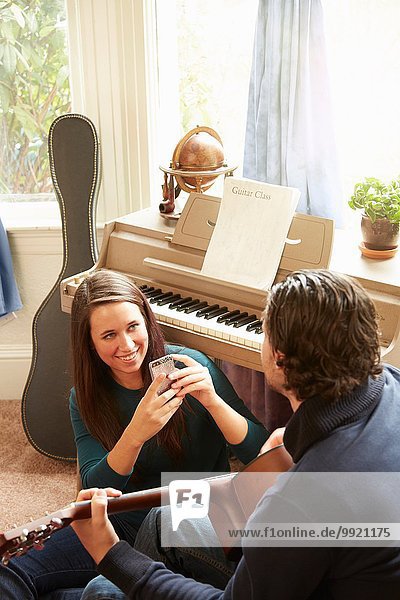Over shoulder view of young woman photographic guitarist boyfriend on smartphone