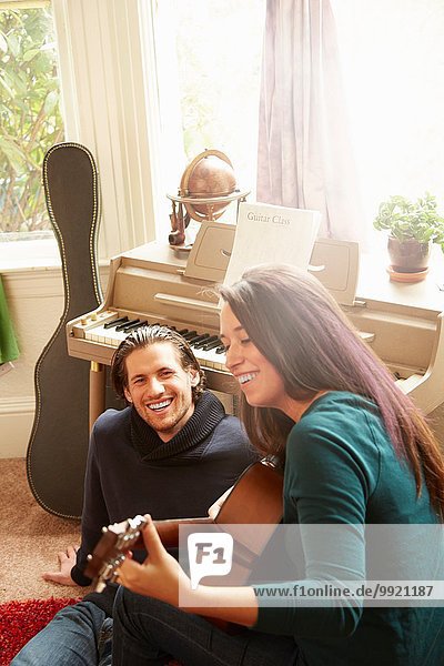 Junges Paar spielt Akustikgitarre im Wohnzimmer