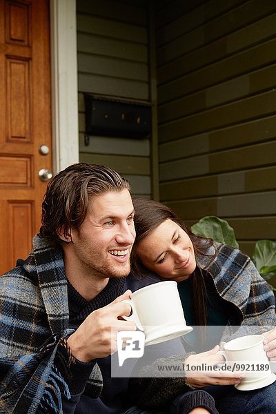 Young couple sitting on porch step wrapped in blanket