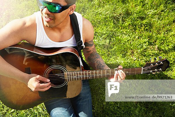 Junger Mann sitzt auf Gras und spielt Akustikgitarre.
