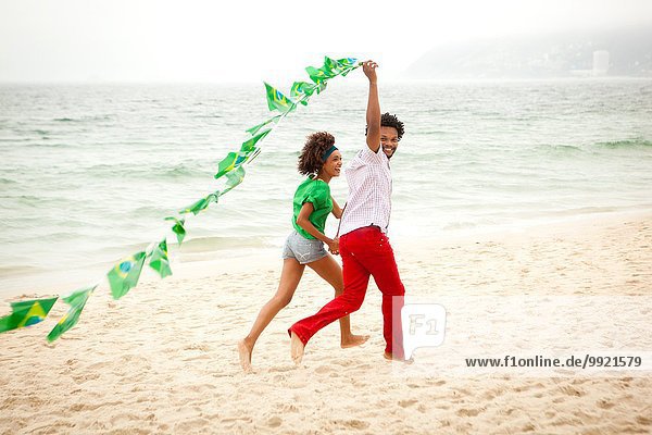 Couple playing with string of flags on beach  Rio de Janeiro  Brazil