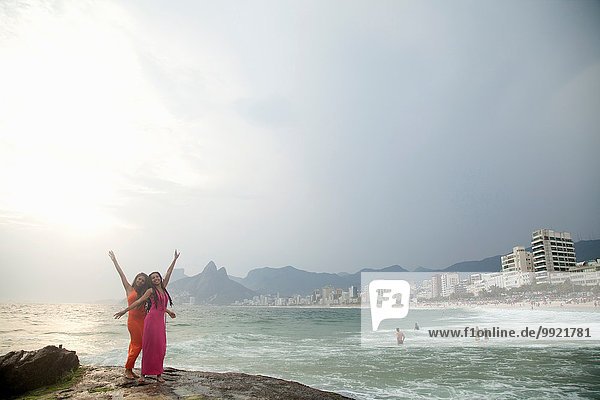 Portrait of two young women with arms raised on Ipanema beach  Rio De Janeiro  Brazil