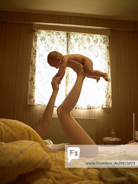 Mother lying on bed balancing baby son on feet