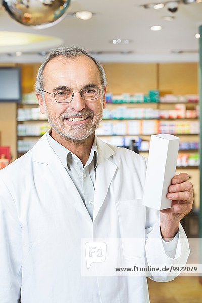 Portrait of senior male pharmacist holding up medicine in pharmacy