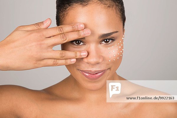 Porträt einer jungen Frau  die das Gesicht mit der Hand berührt  Punkte von Schönheitscreme auf der Wange