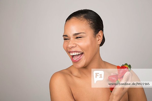 Porträt einer jungen Frau  lachend  mit einer Handvoll Erdbeeren in der Hand.