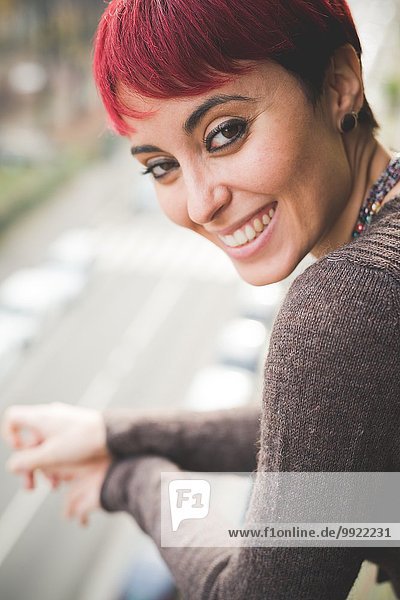Junge Frau an Balkongeländer gelehnt  lächelnd