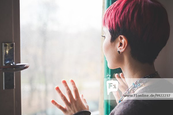 Junge Frau schaut aus dem Fenster  Hände berühren Fenster  Rückansicht