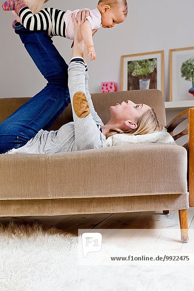 Mother lying on sofa  holding baby girl in air