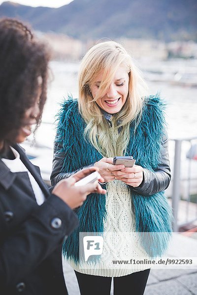 Zwei junge Frauen texten auf Smartphones am Comer See  Comer See  Italien