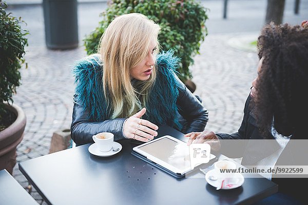 Zwei junge Frauen  die ein digitales Tablett im Straßencafé  Comer See  Comer See  Italien  benutzen.