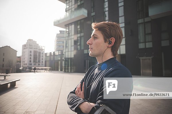 Young male runner listening to earphones in city square