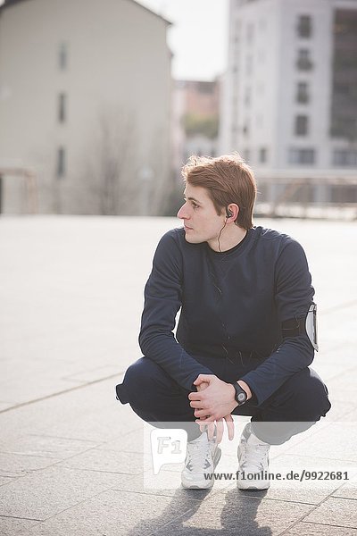 Young male runner crouching in city square
