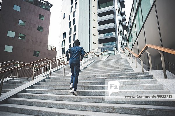 Rückansicht des jungen männlichen Läufers  der die Stadttreppe hinaufläuft.