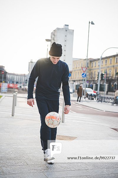 Young male soccer player playing keepy uppy on city street