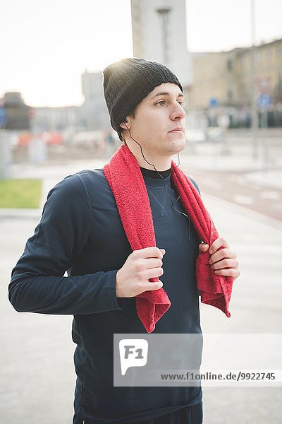 Young male runner with towel around his neck taking a break in city
