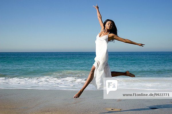 Junge Tänzerin springt am Strand in die Luft