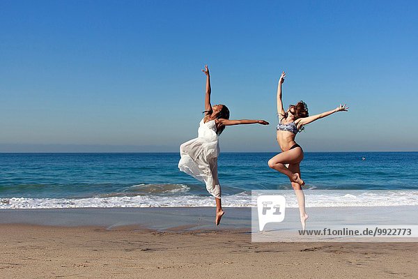Zwei junge Tänzerinnen  die am Strand in die Luft springen