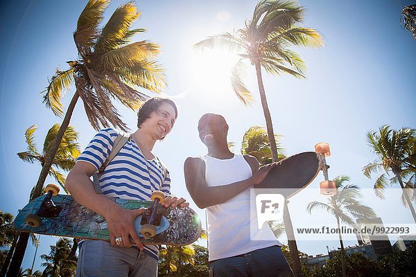 Zwei Männer  die Skateboards in der Hand halten und im Freien spazieren gehen