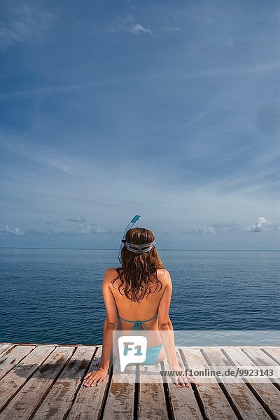 Mittlere erwachsene Frau auf dem Pier sitzend mit Blick aufs Meer